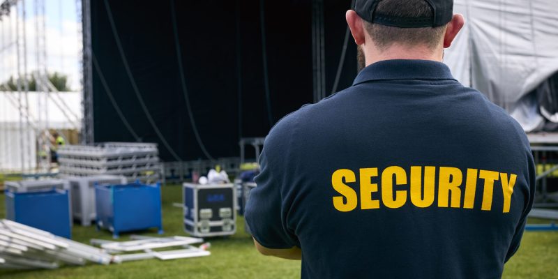 Rear View Of Security Team At Outdoor Stage For Music Festival Or Concert